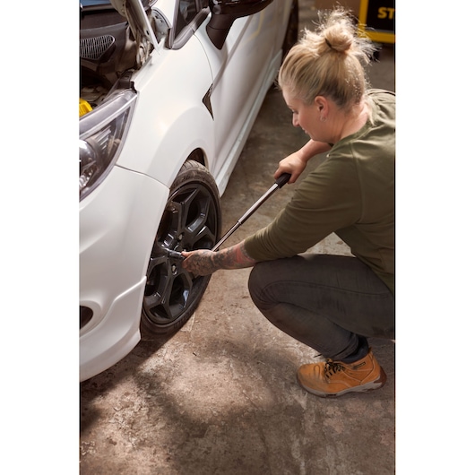 STANLEY STHT80890-0 torque wrench used on car wheel, side angle, person kneeling, garage setting.