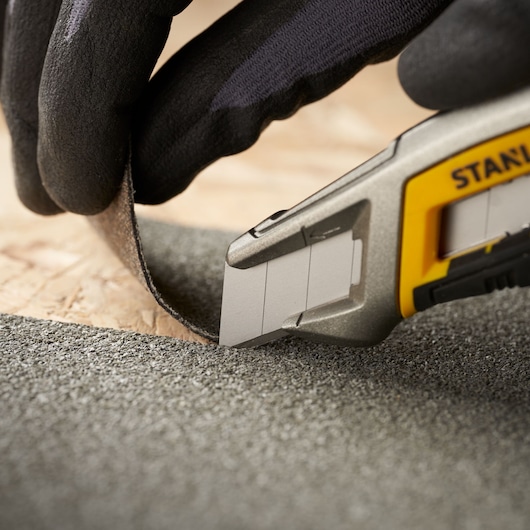 Photo of STANLEY STHT9-11301 utility knife cutting abrasive material, close-up side angle.