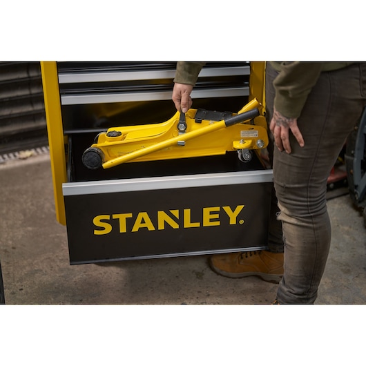 STANLEY STMT81251-1 tool chest with yellow floor jack in open drawer, person holding jack handle.