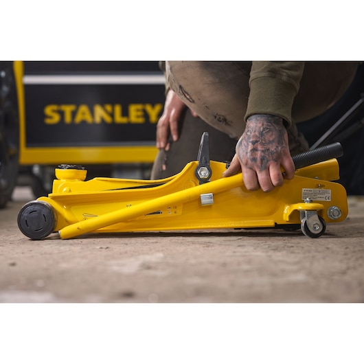 STANLEY STMT81251-1 yellow hydraulic floor jack in use, side view, on rough ground.