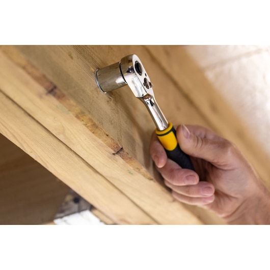 STANLEY STMT82663-0 ratchet wrench with yellow and black handle in use tightening bolt on wood.