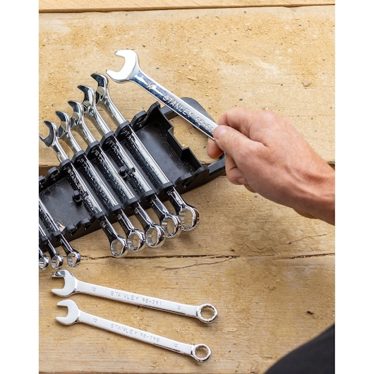 STANLEY STMT82842-0 wrench set in black holder, hand holding one chrome wrench, two wrenches on wooden surface.