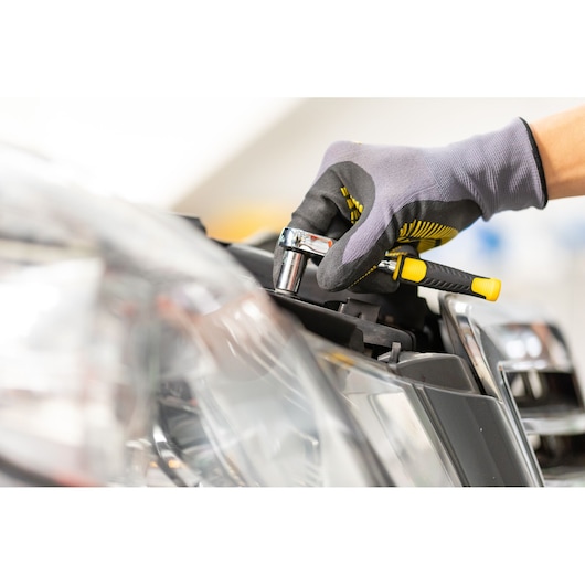 STANLEY STMT86112-0 ratchet used on car headlight, close-up, yellow black handle, mechanic’s glove.