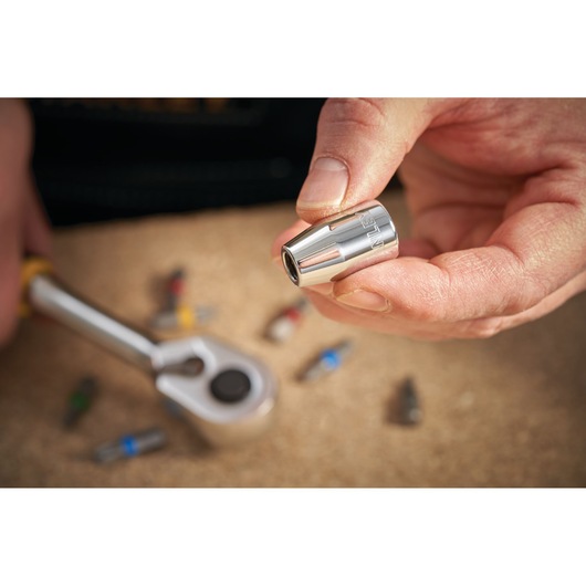 Photo of STANLEY STMT86250-0 socket bit held by hand, ratchet and bits on work surface.