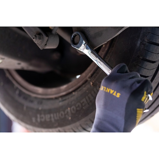 STANLEY STMT89910-0 wrench in use on car undercarriage, user wearing STANLEY gloves, photography close-up.