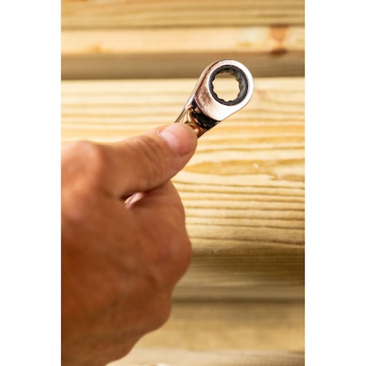 STANLEY STMT89918-0 ratcheting wrench held in hand, close-up against wooden planks, photography category.