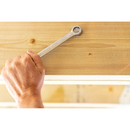 STANLEY STMT95910-0 ratcheting wrench held by hand against light wood surface, side angle.