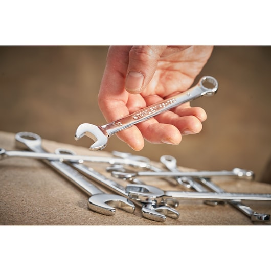 Photo of STANLEY STMT95912-0 chrome combination wrench held in hand with other wrenches on table.
