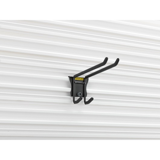 STANLEY STST82606-1 black steel wall hook with two prongs, mounted on white ribbed wall, front angle.