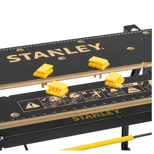 STANLEY STST83800-1 workbench close-up with black surface, yellow clamps, and measurement markings.