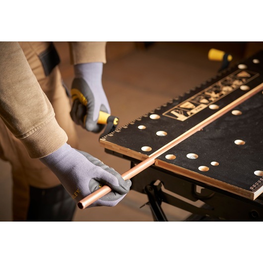 STANLEY STST83800-1 workbench photography showing gloved hands cutting copper pipe on black surface.