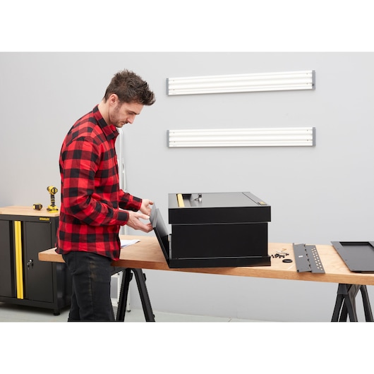 Photo of STANLEY STST97599-1 storage box assembly on wooden table, black metal panels and parts visible.