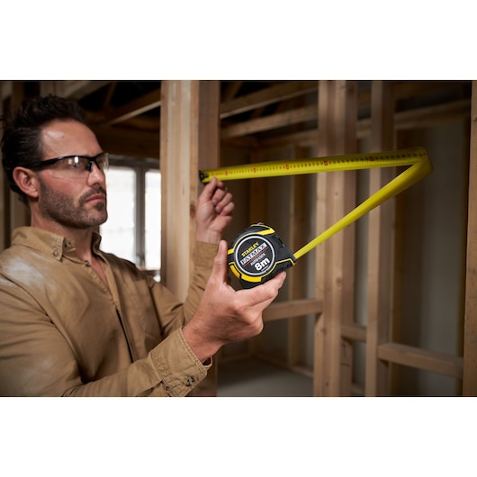 Photo of STANLEY XTHT0-33501 tape measure in use, yellow blade extended at a construction site.