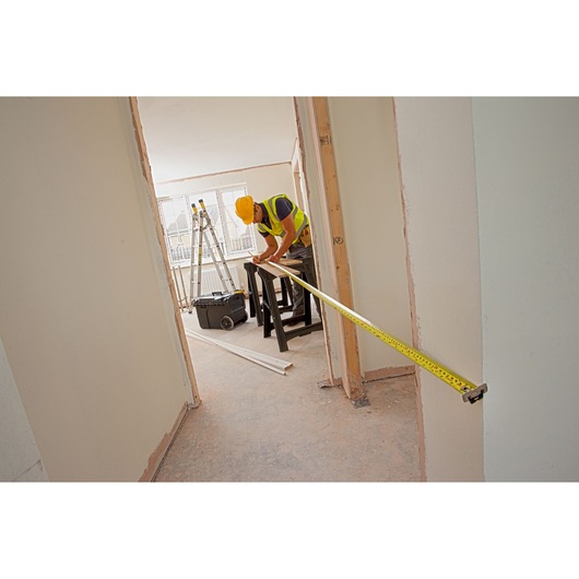 STANLEY XTHT0-33503 tape measure used by worker in construction setting, extended across doorway.