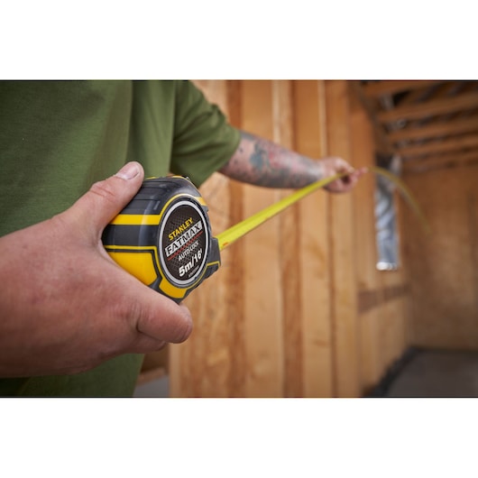 Photo of STANLEY XTHT0-33503 FATMAX tape measure in use, extended inside a wooden construction frame.