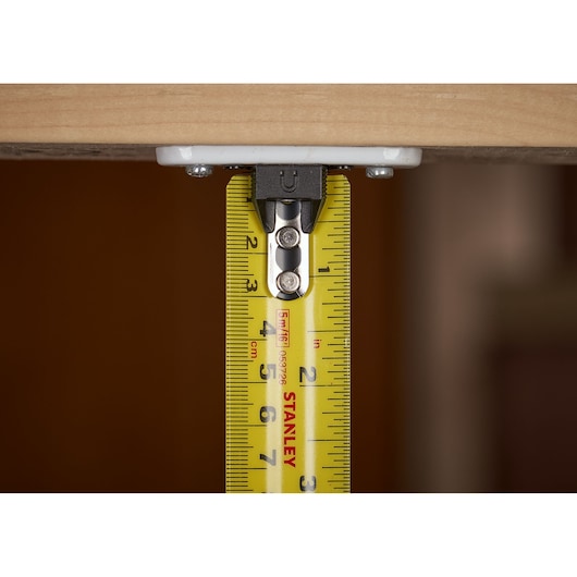 STANLEY XTHT0-33503 tape measure under wood surface, close-up showing yellow blade and measurements.