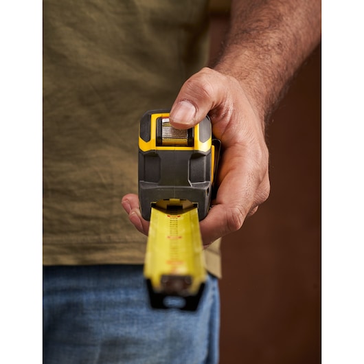 STANLEY XTHT0-33671 tape measure held in hand, yellow and black casing, extended measuring blade, close-up front view.